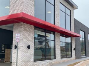 a flat red metal awning wrapping around two sides of a building, shielding large windows beneath