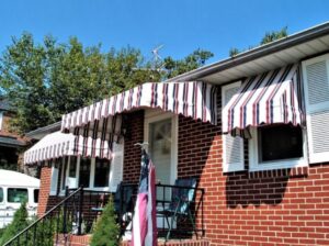 a small home with white red and blue multi-stripe awnings hang over two windows and an entrance